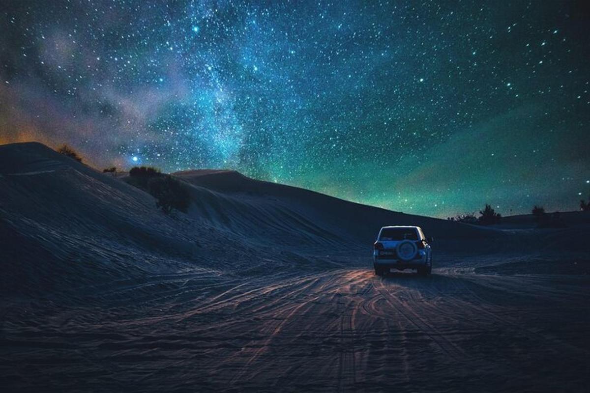 ein Auto, das unter einem Sternenhimmel eine unbefestigte Straße entlangfährt