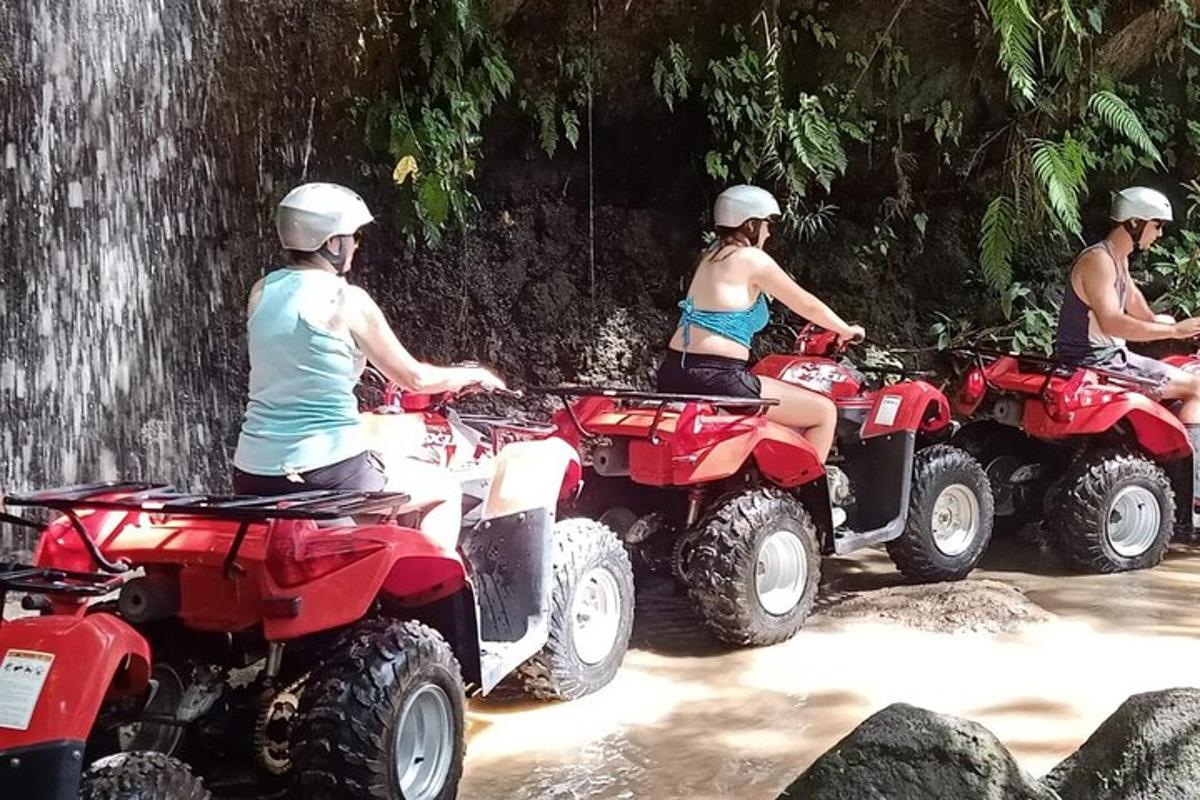 três pessoas andando de quadriciclo em frente a uma cachoeira