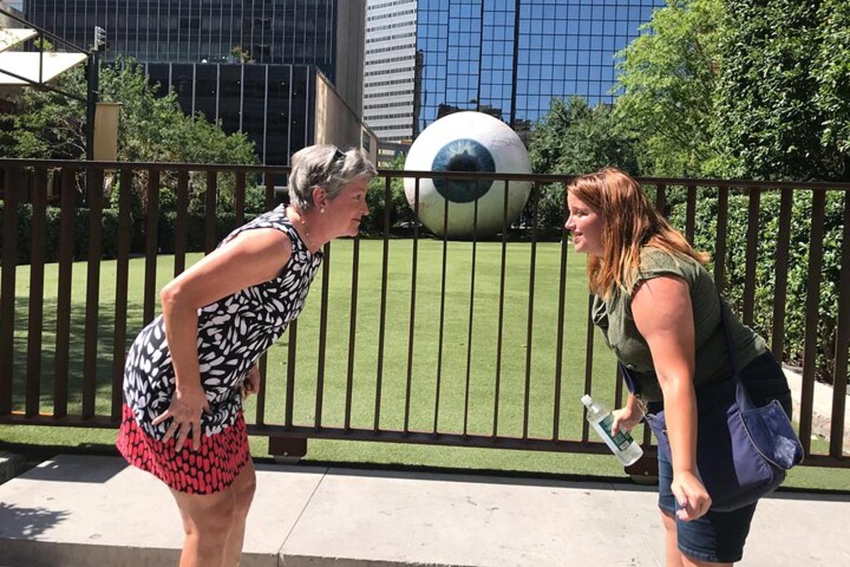 two women walking down a sidewalk in front of a sculpture