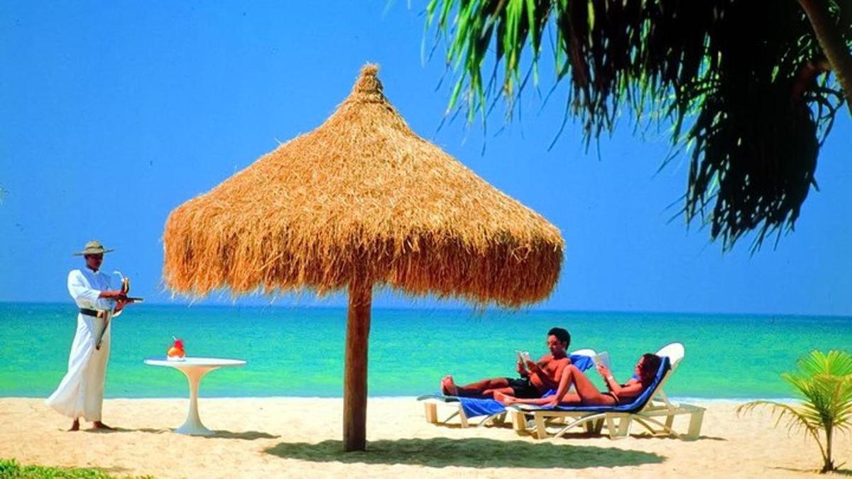 dua orang duduk di kerusi di bawah payung jerami di pantai