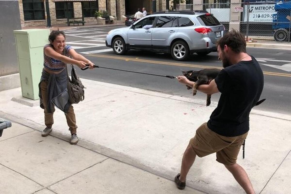 un uomo e una donna che giocano con un cane su un marciapiede