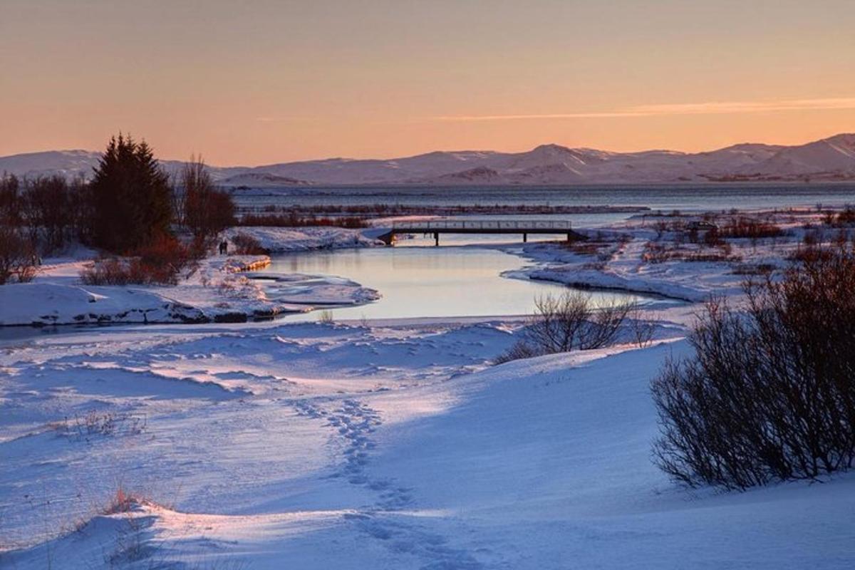 una scena invernale di un fiume con neve e montagne