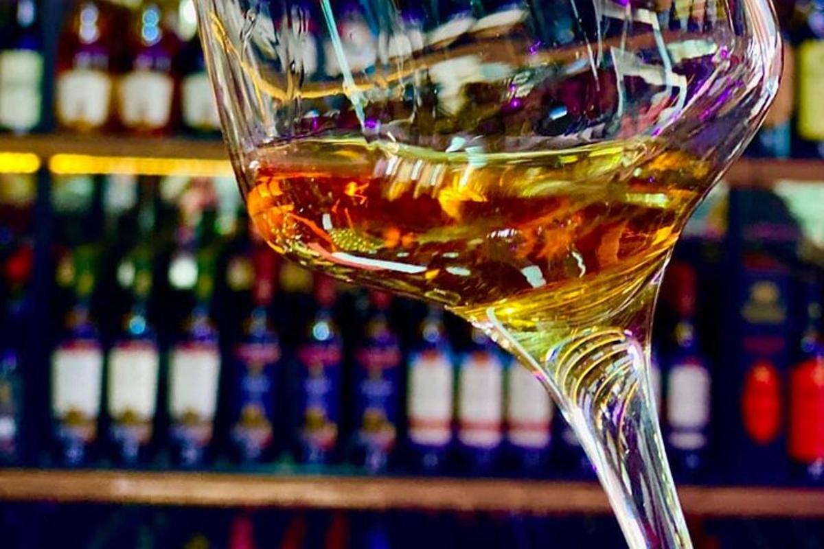 Un vaso de whisky delante de un estante de botellas