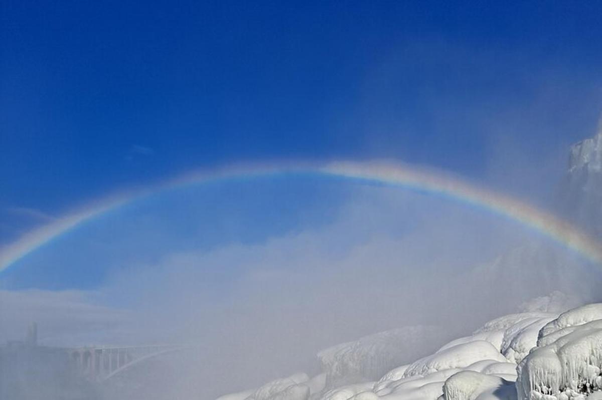a rainbow in the sky over a snow covered mountain