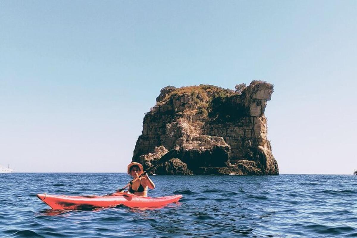 Una niña en un kayak rojo en el océano con una roca.
