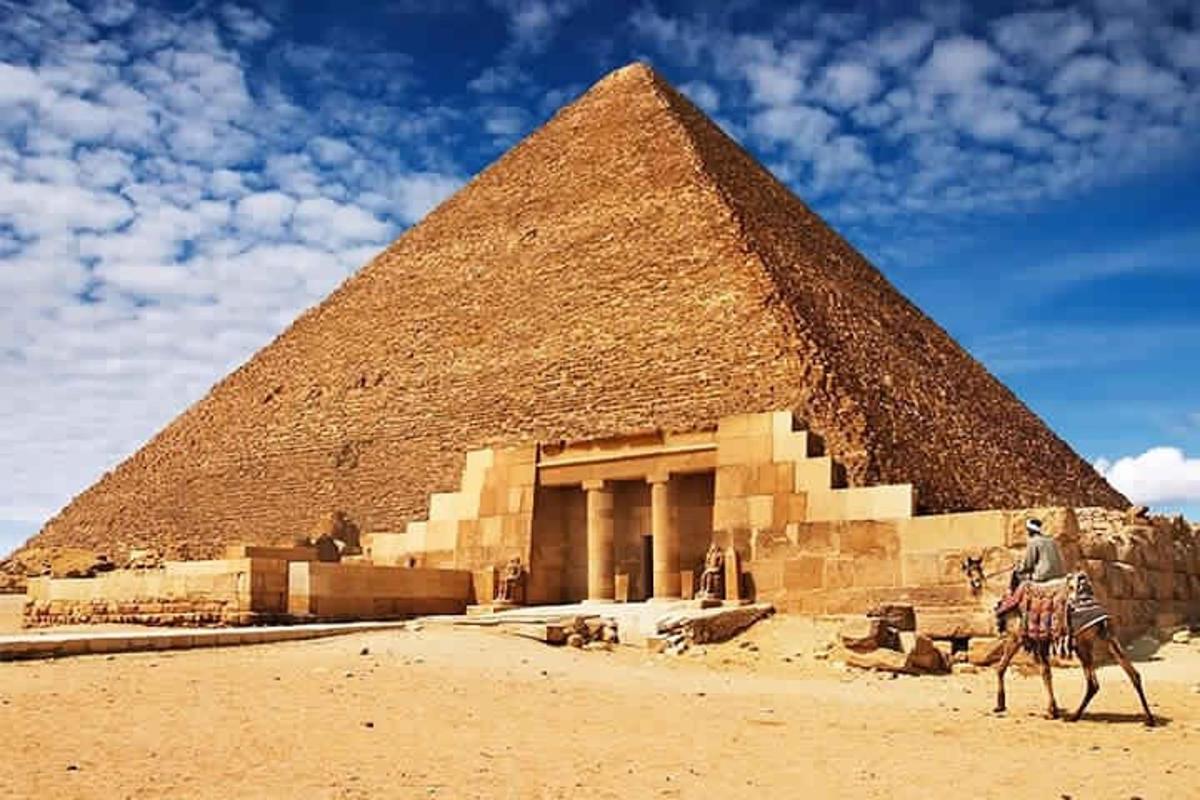 muž jedoucí na velbloudovi před pyramidou