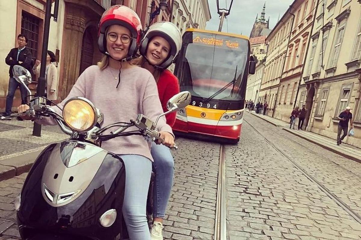 dvi moterys sėdi ant motorolerio priešais tramvajų