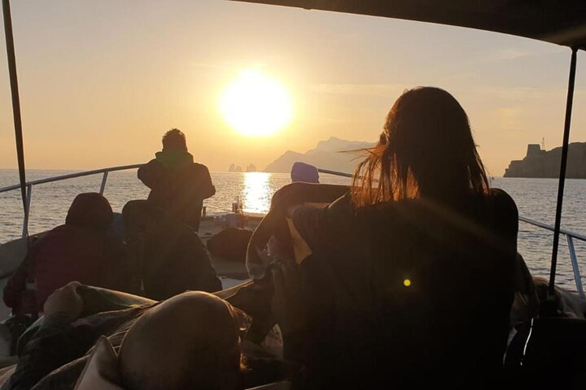 un grup de persones assegudes en un vaixell mirant la posta de sol