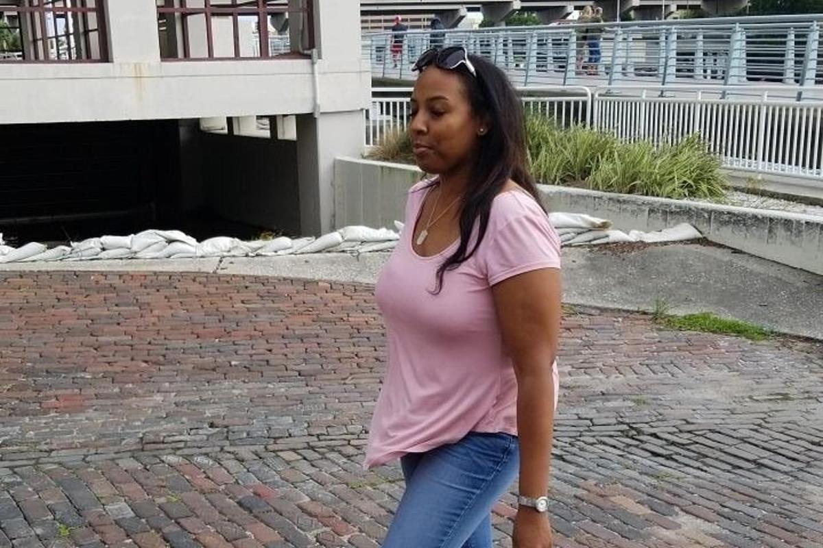 o femeie într-o cămașă roz mergând pe o stradă cu cărămizi
