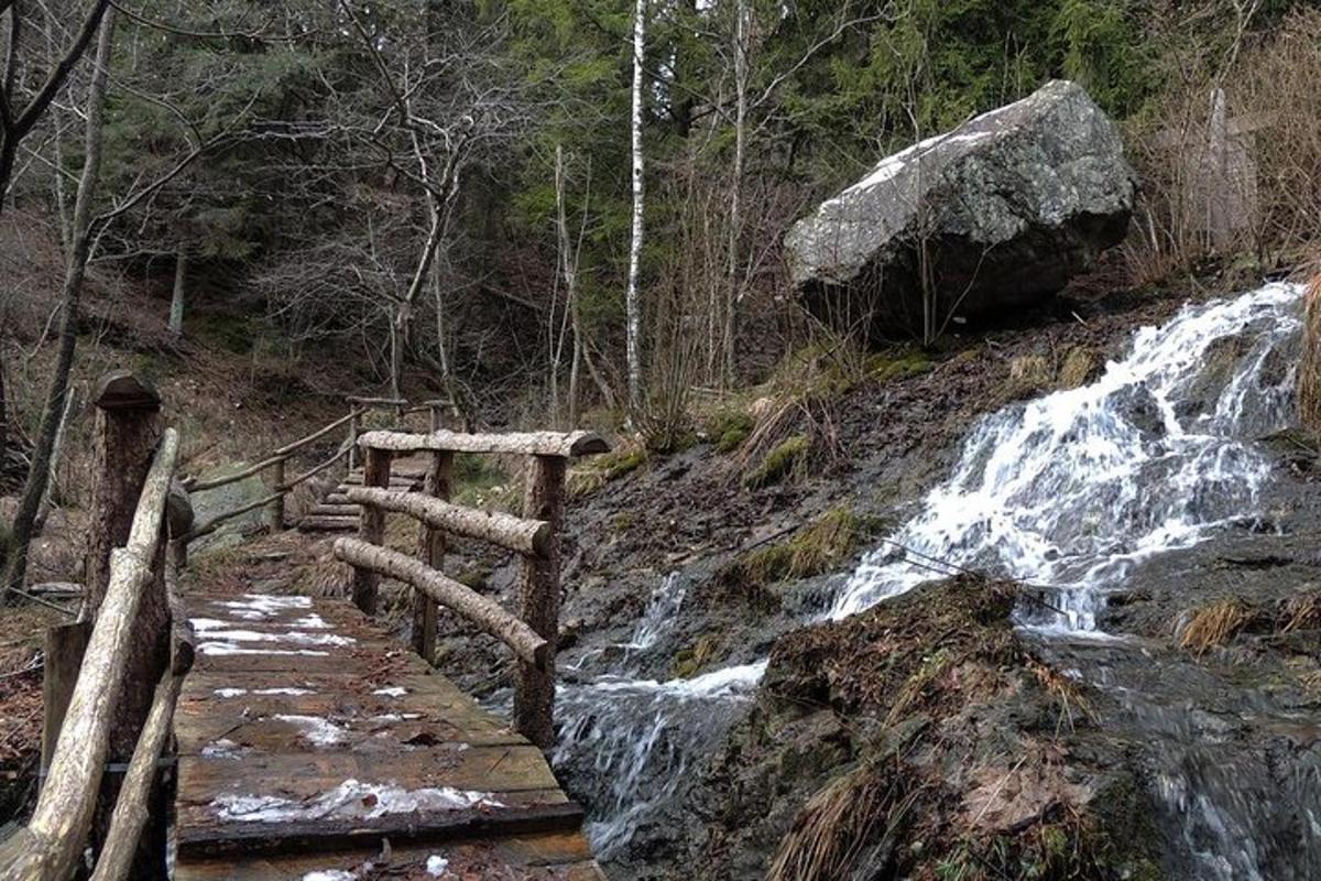 a waterfall on a hill with a wooden bridge next to a river