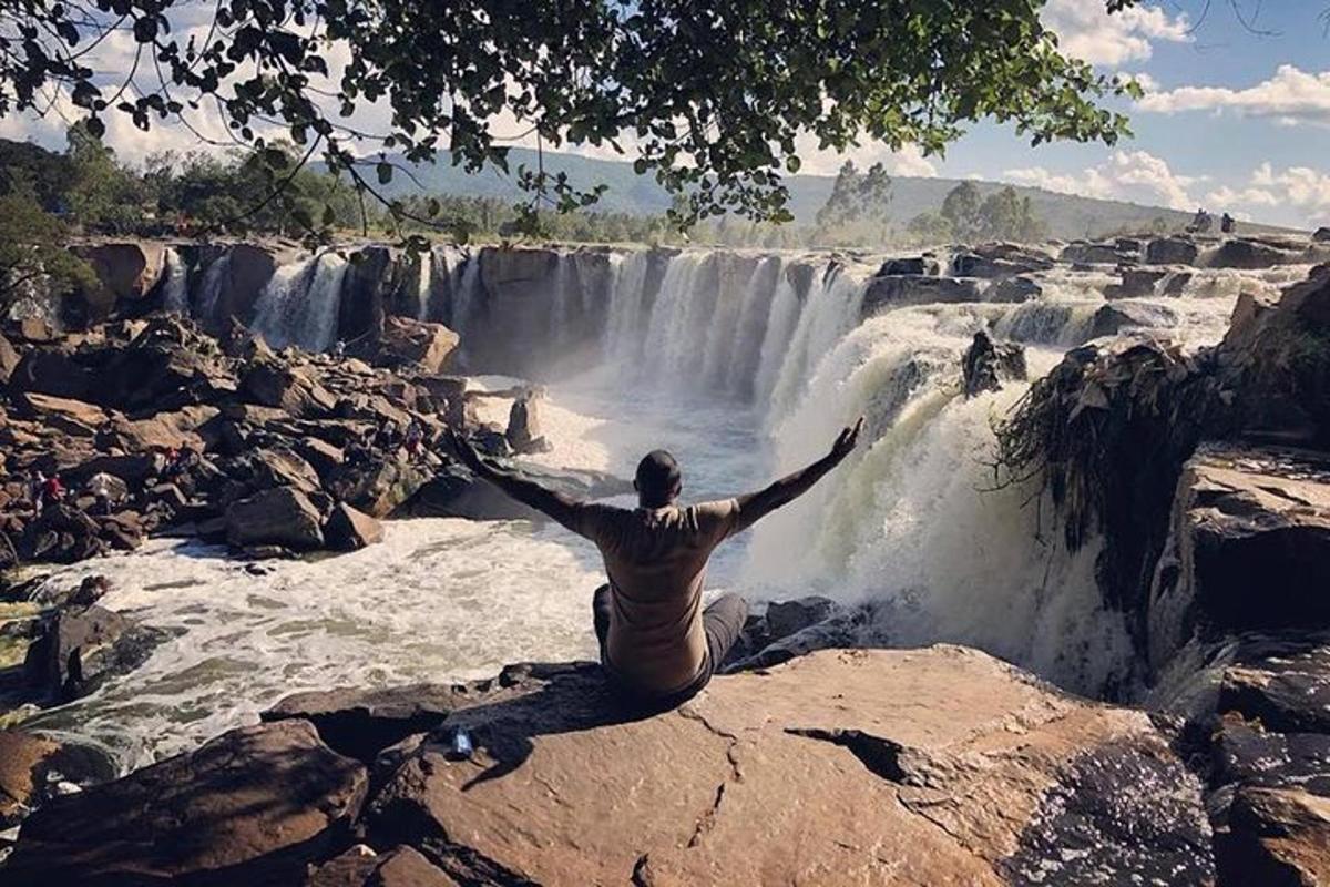a man sitting on a rock in front of a waterfall