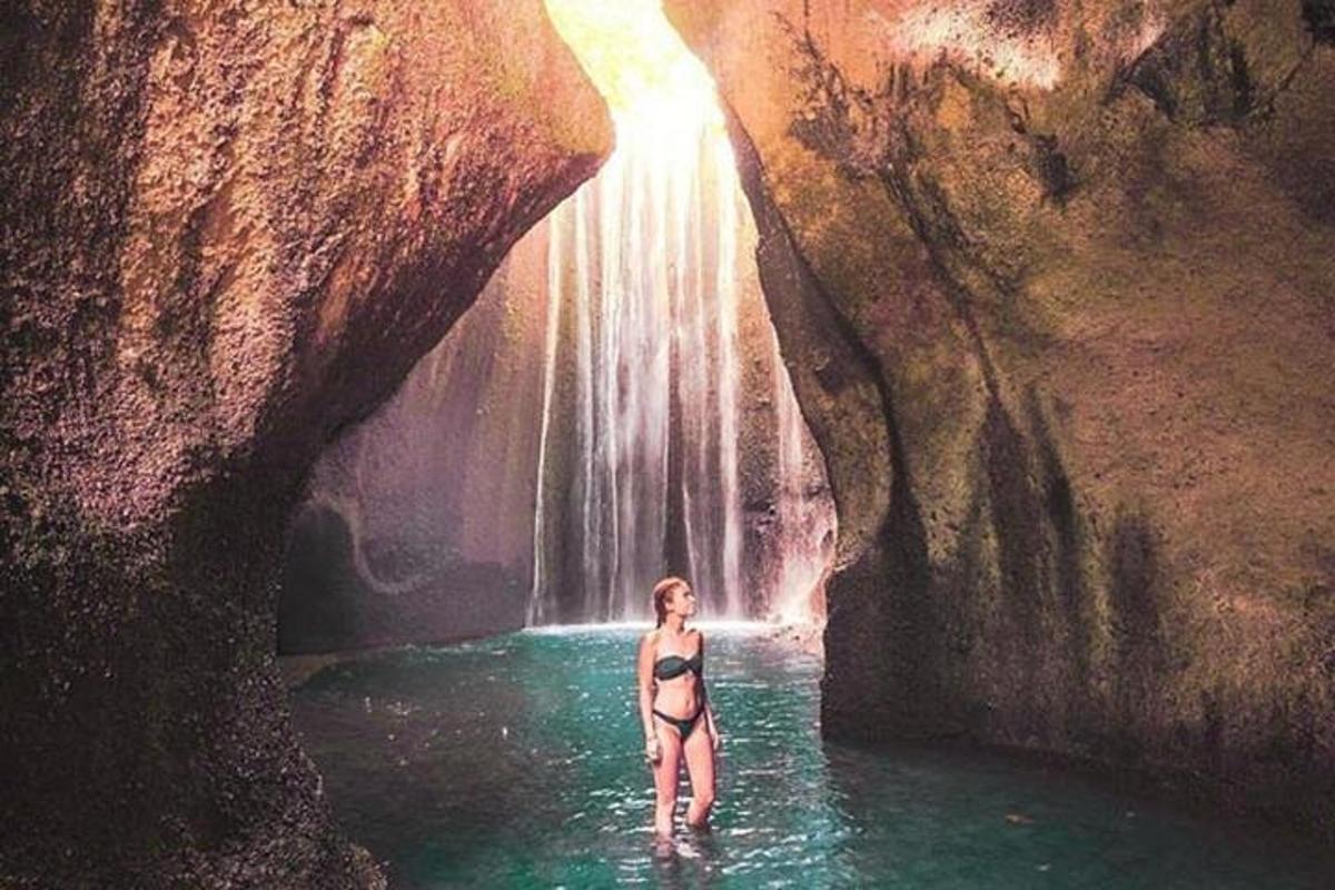 kona stendur í vatnspolli við foss