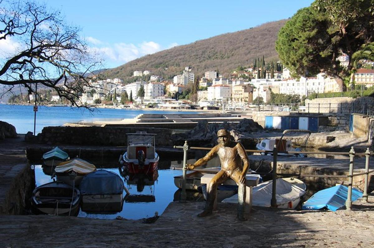 una estàtua d'un home assegut en un moll al costat de vaixells