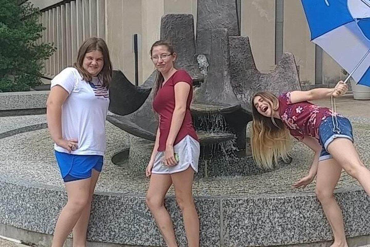 three women standing in front of a fountain with umbrellas