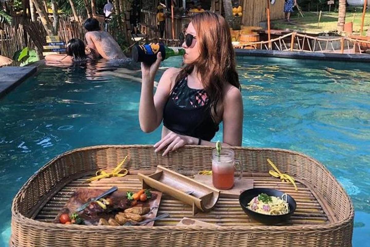 một người phụ nữ đang ngồi trong hồ bơi uống một ly nước