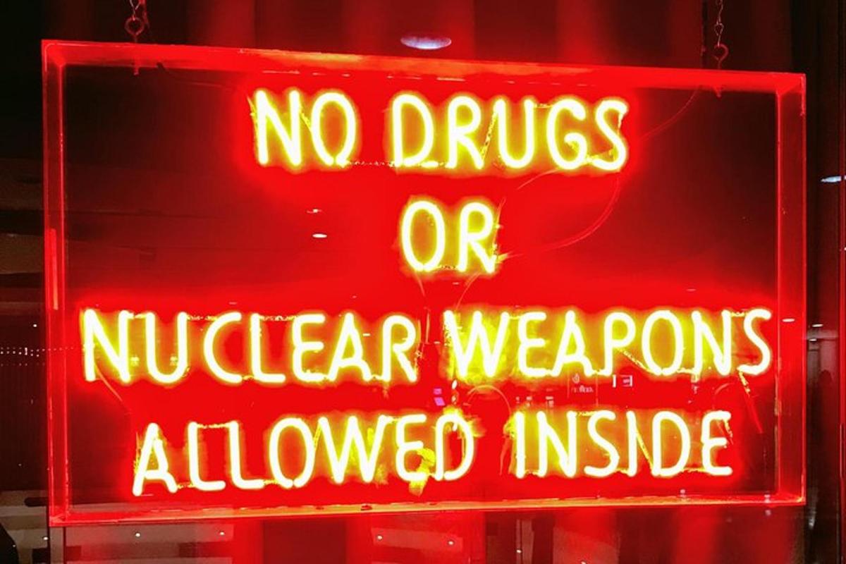 een neonbord met de tekst 'geen drugs of kernwapens toegestaan'