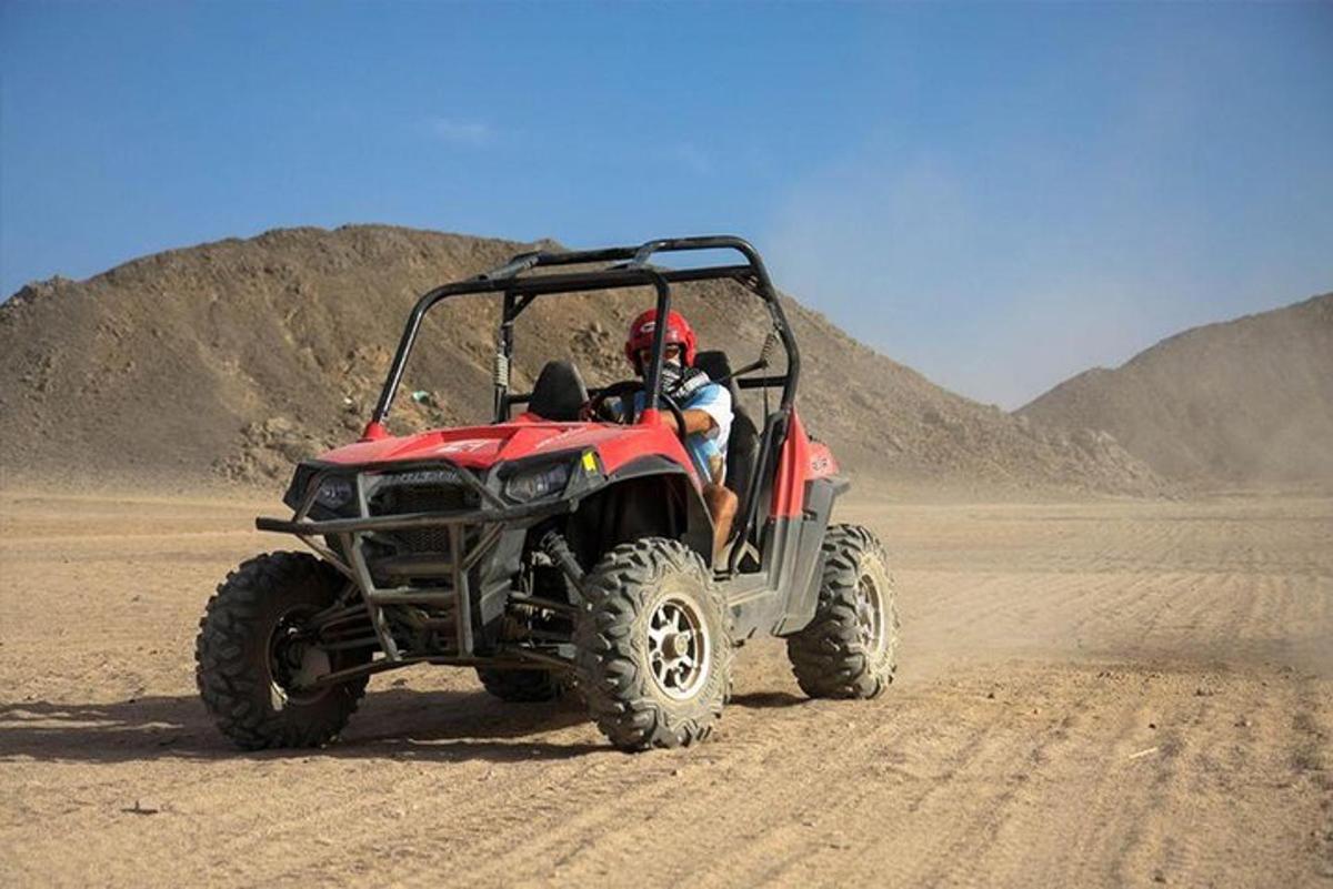 um homem dirigindo um quadriciclo vermelho no deserto