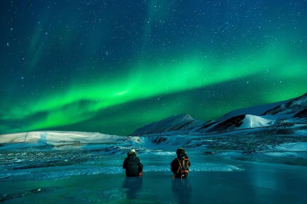 Tveir menn sitja á ís undir norðurljósum