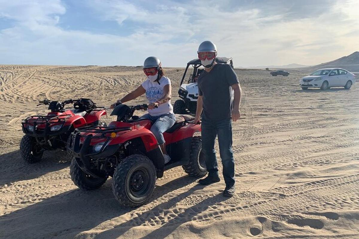 um homem e uma mulher parados ao lado de um quadriciclo no deserto