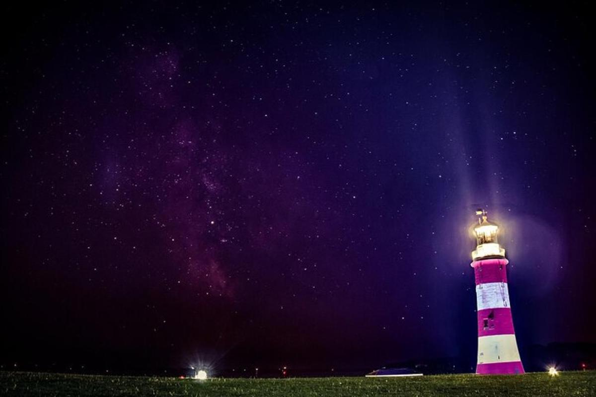 a lighthouse lit up at night with the stars in the sky