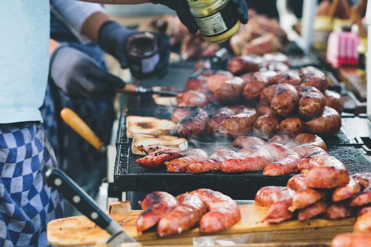 a person cooking meat and sausages on a grill