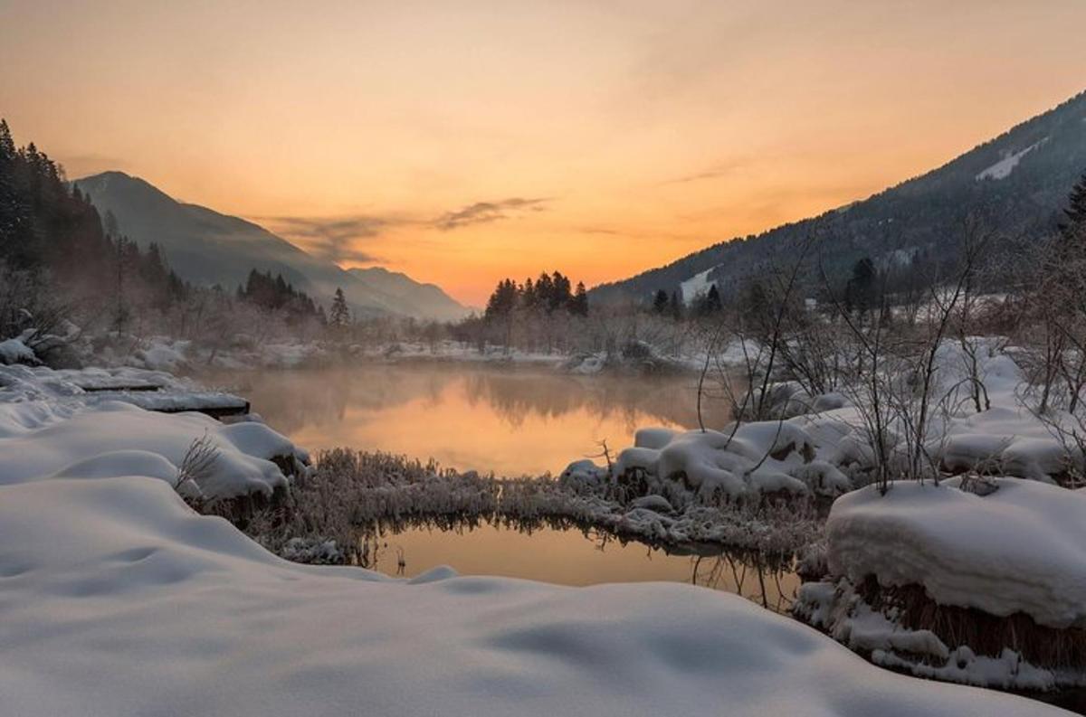 un fiume coperto di neve con un tramonto sullo sfondo
