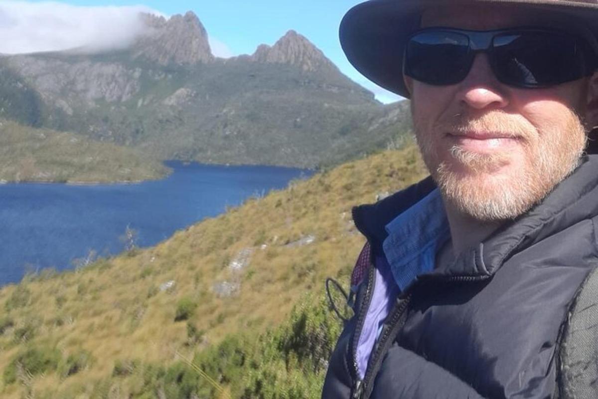 un uomo che indossa occhiali da sole e un cappello in piedi su una montagna