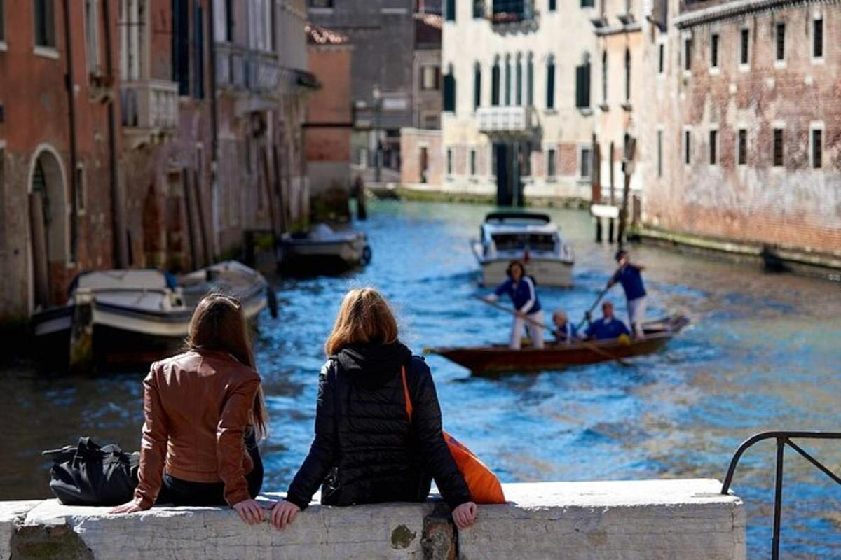due donne sedute su un muro che guardano le barche in un canale