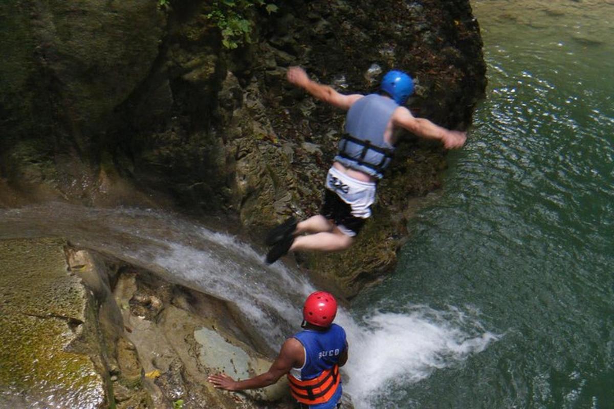 two people jumping off of a waterfall into a river