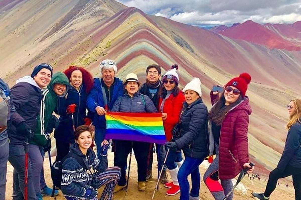 un gruppo di persone che tengono una bandiera arcobaleno di fronte a una montagna
