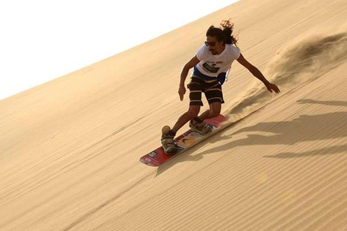 Una mujer bajando una patineta por una colina de arena