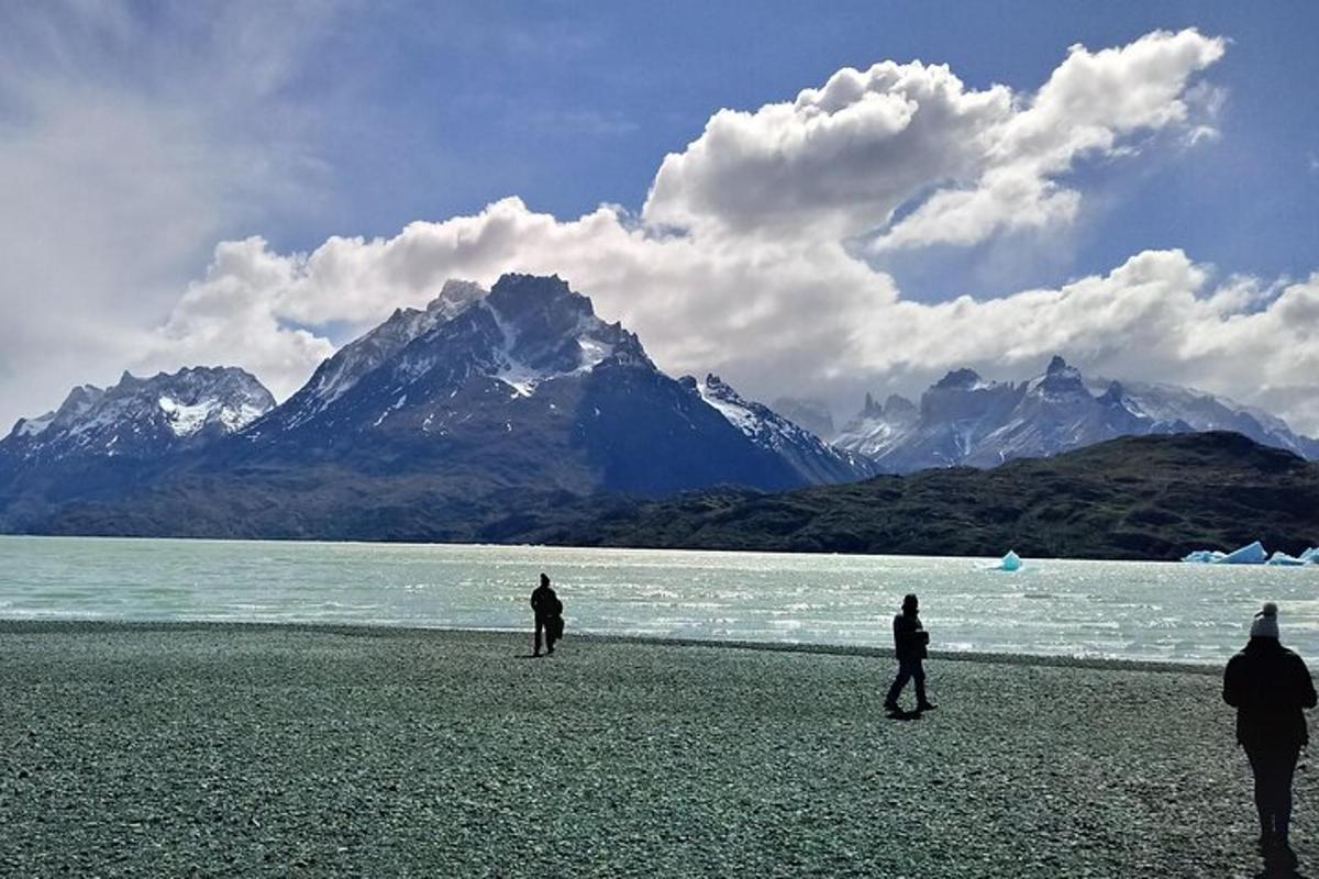 three people walking on a beach with mountains in the background