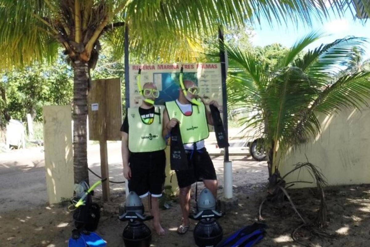 two men standing in front of a sign next to a palm tree