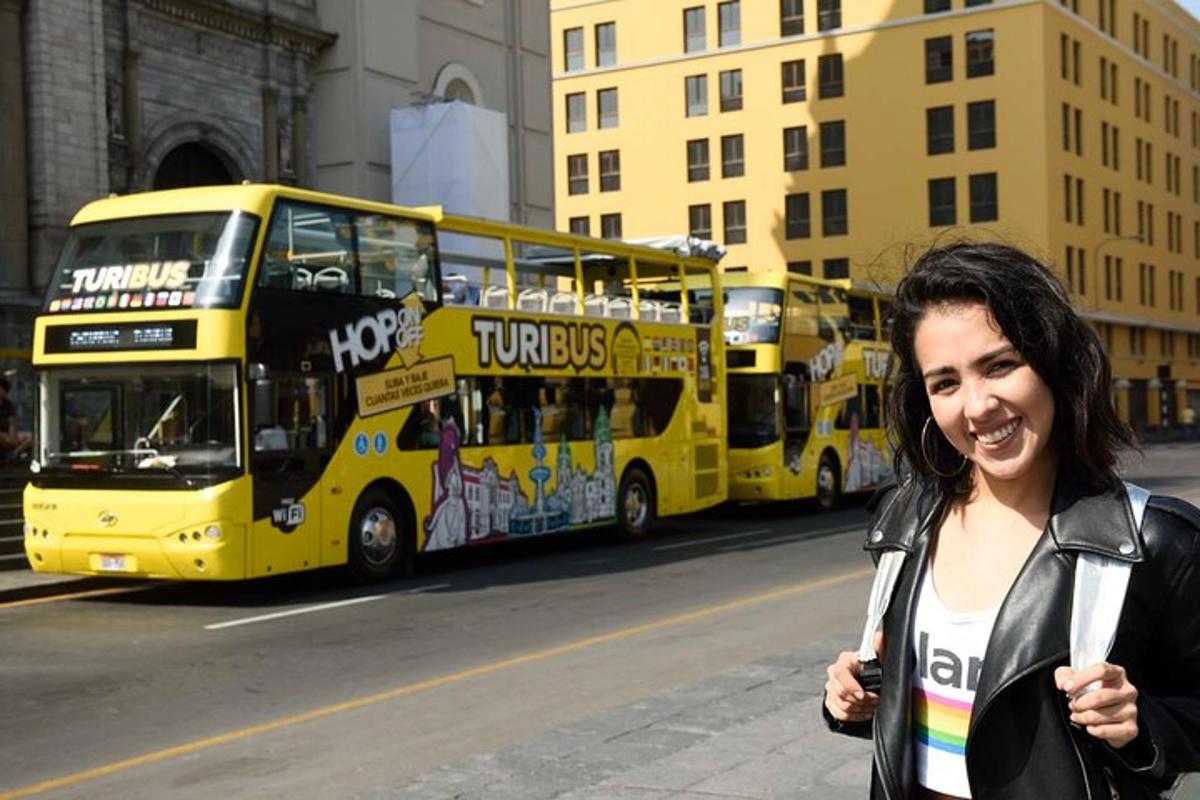 Una mujer parada frente a un autobús amarillo de dos pisos.