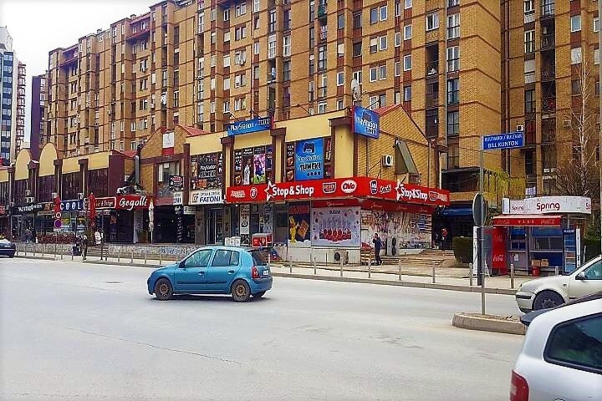 a small blue car driving down a street with buildings