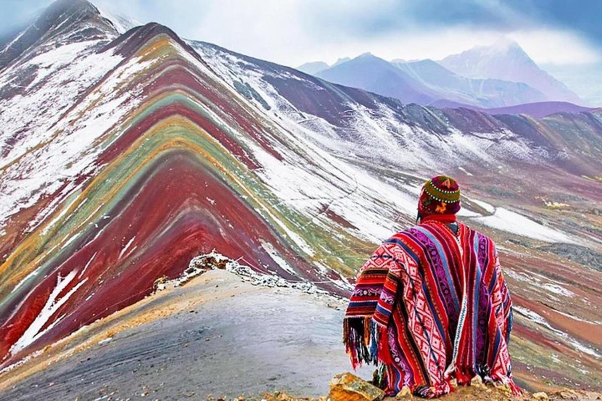 um homem sentado no topo de uma montanha olhando para uma montanha coberta de neve