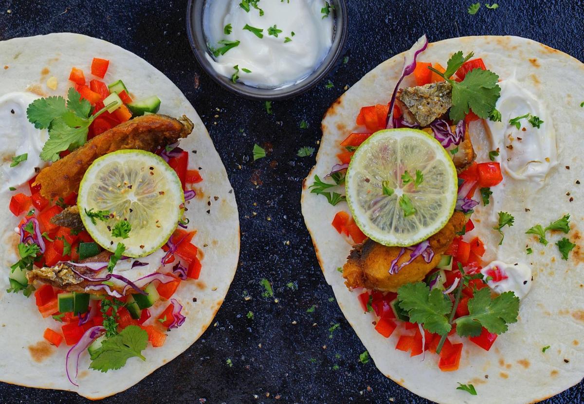 Dos tacos con pescado y verduras en una mesa.