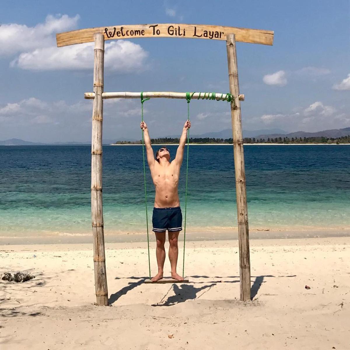 a man standing under a wooden sign on the beach