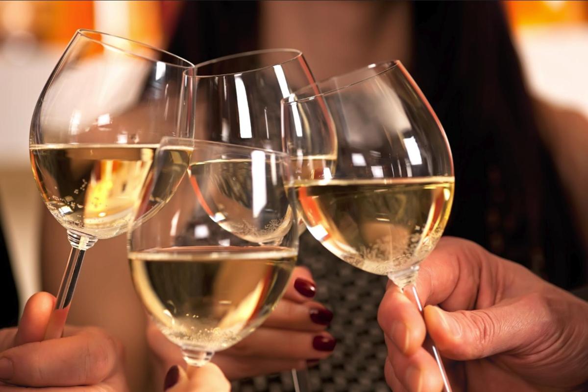 three people holding up four glasses of white wine