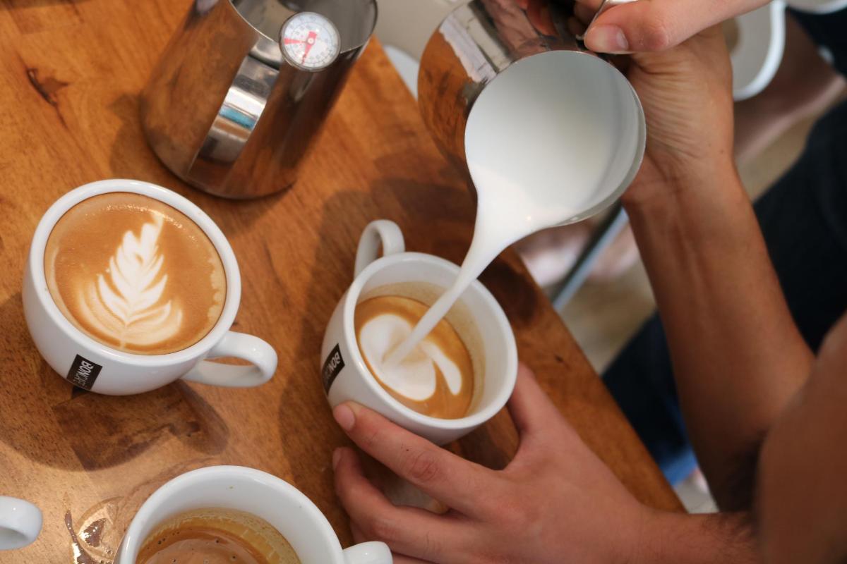 una persona vertiendo leche en una taza de café