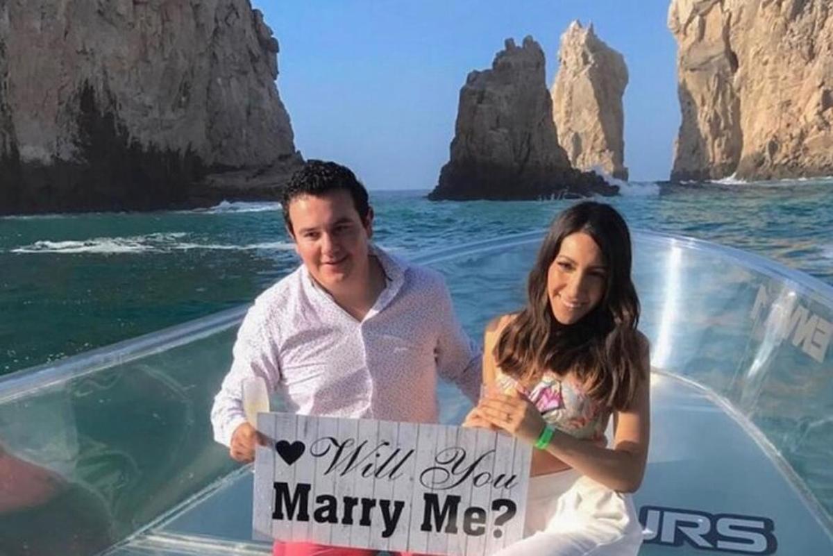 un bărbat și o femeie care țin un semn „căsătorește-te cu mine” pe o barcă