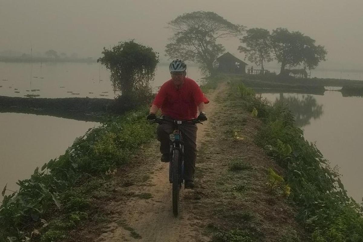 a man riding a bike down a dirt road next to a lake