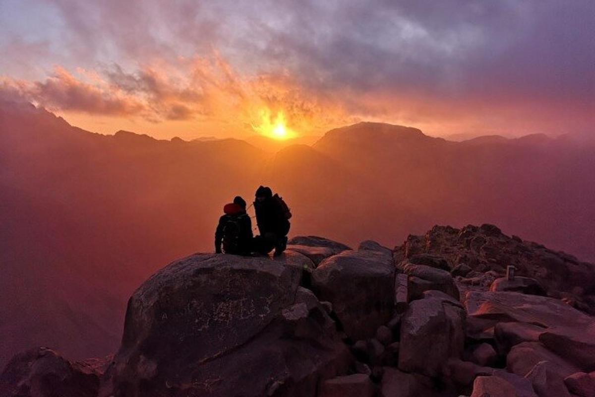 two people sitting on top of a mountain at sunset