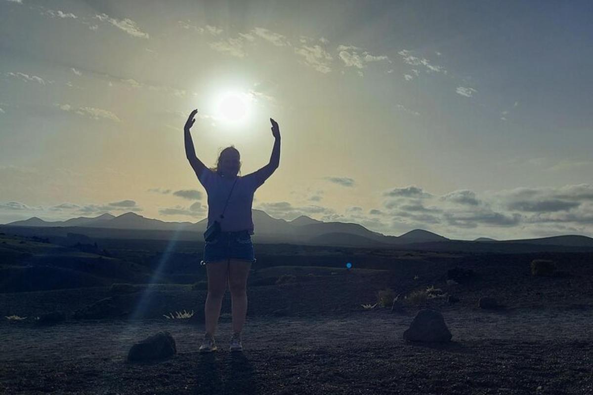 a woman standing on a hill with the sun in the sky