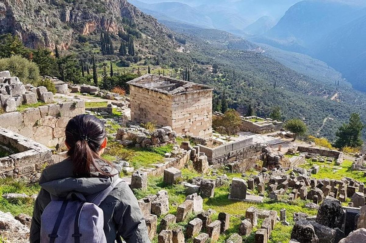 a woman with a backpack standing on a hill looking at a ruins