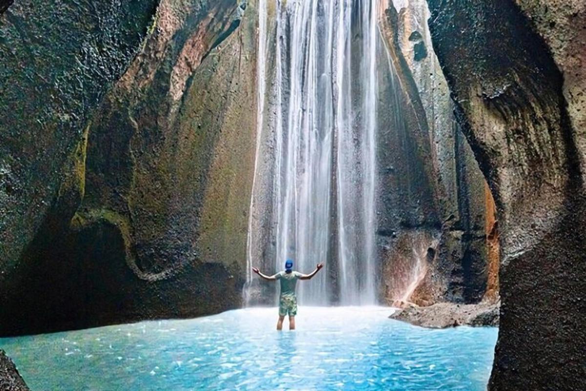 a man standing in water in front of a waterfall
