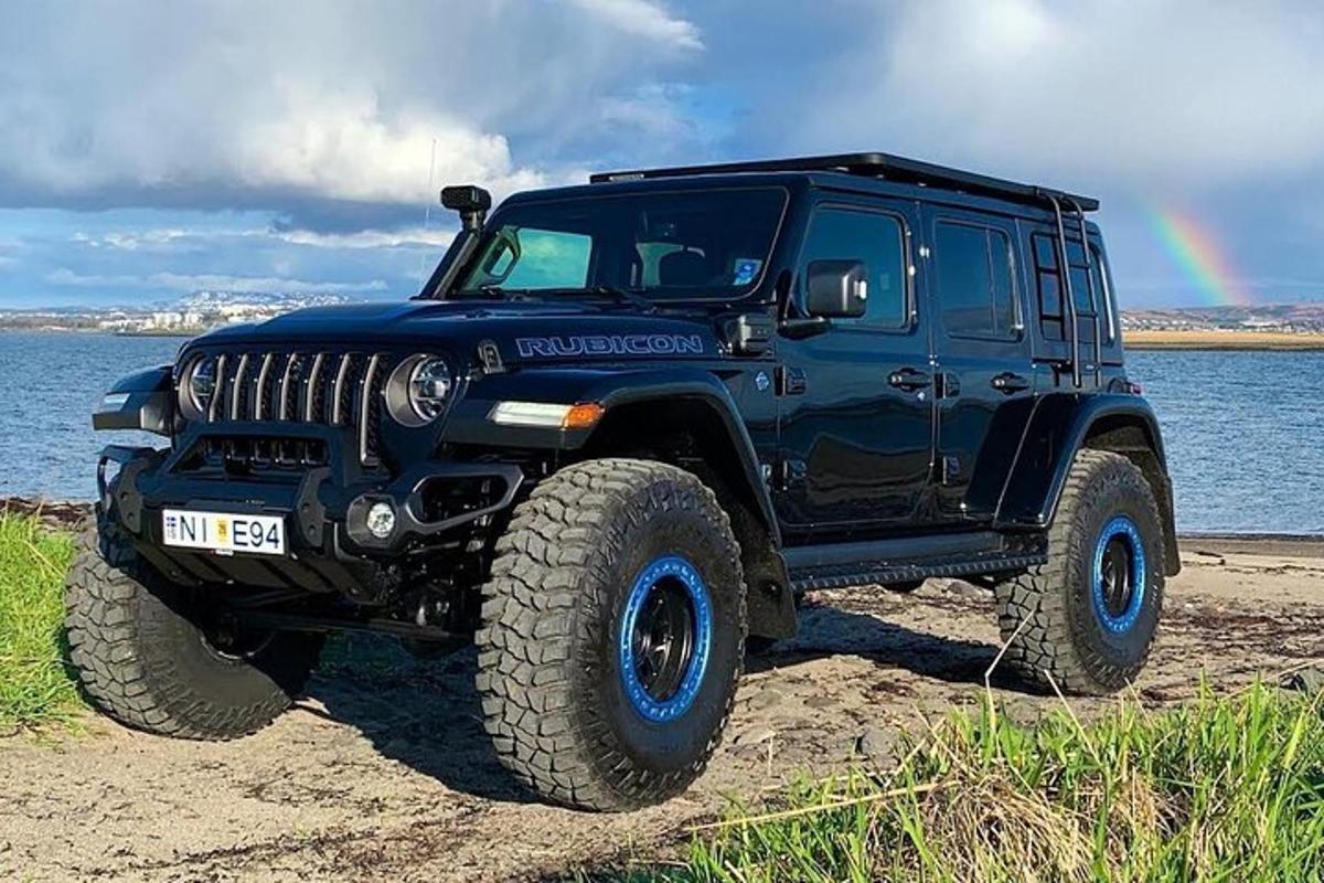 a black jeep parked on the beach with a rainbow in the background