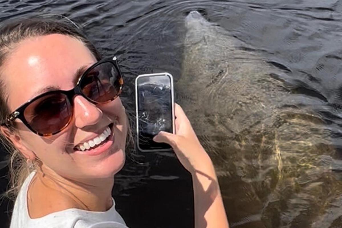 a woman holding up a cell phone in front of a large fish