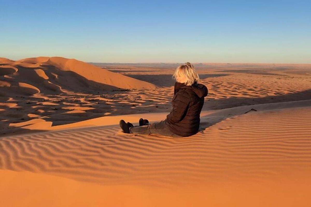 a woman sitting on a sand dune in the desert