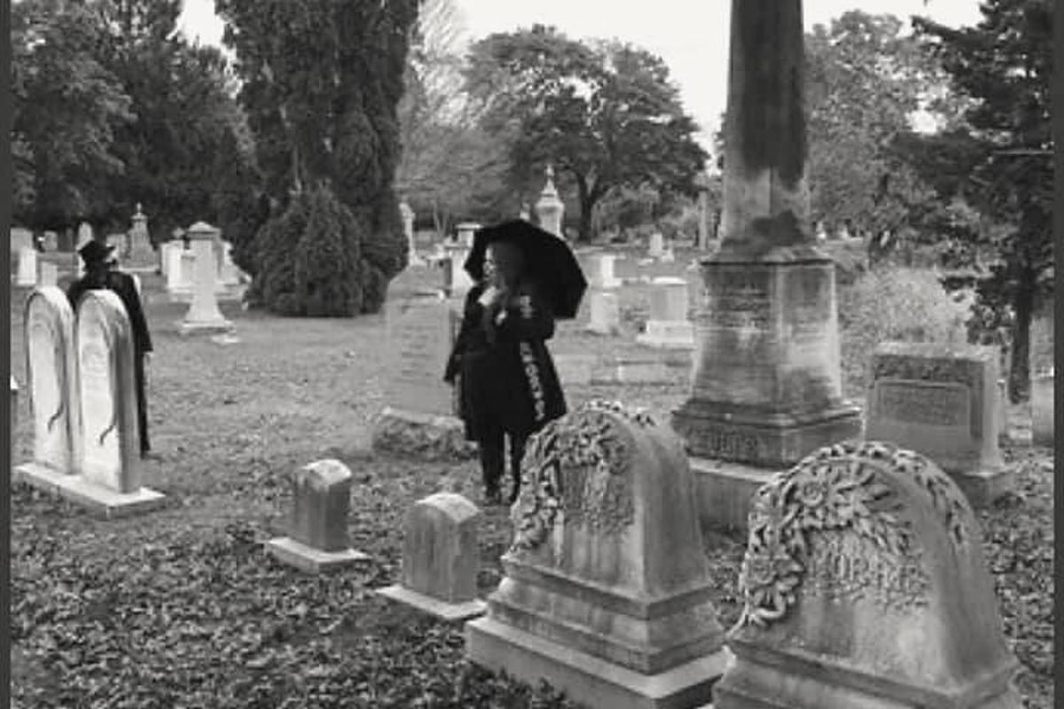 a woman with an umbrella walking through a cemetery